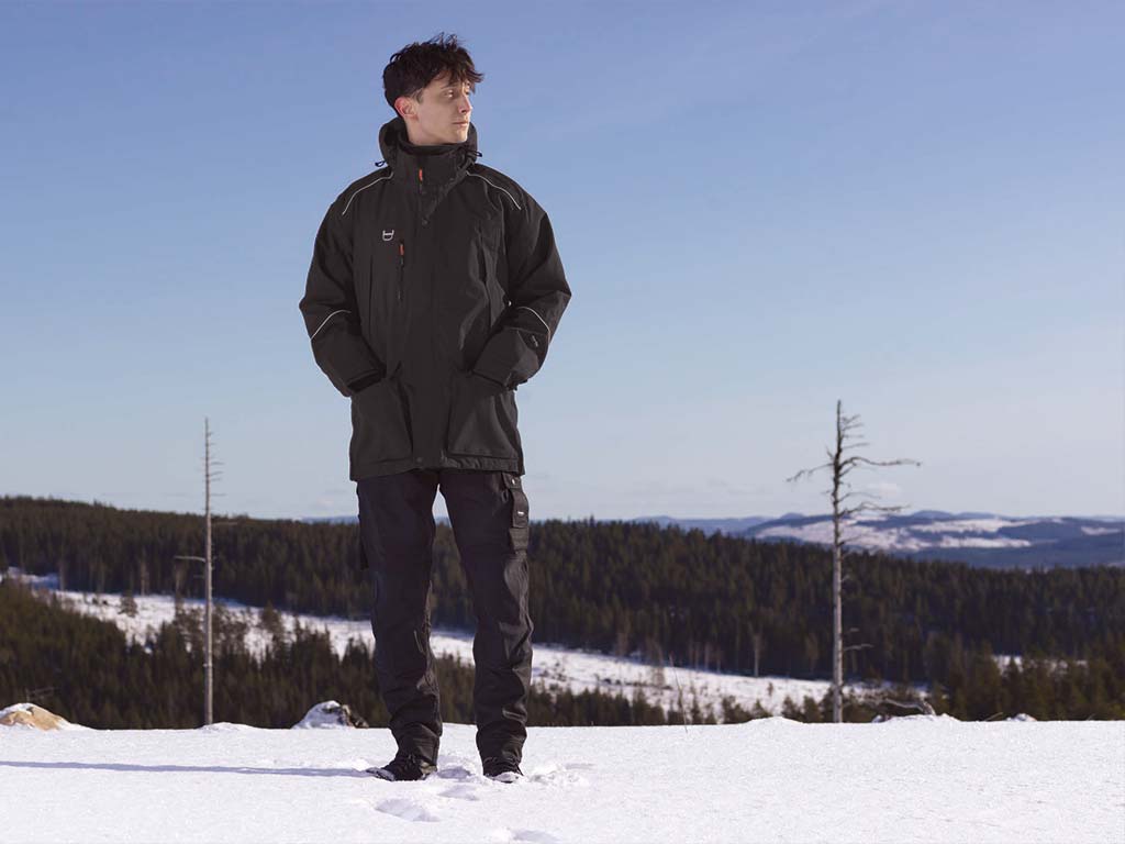 Ein Mann steht gut geschützt mit einer Tranemo-Winterjacke in einer Winterlandschaft
